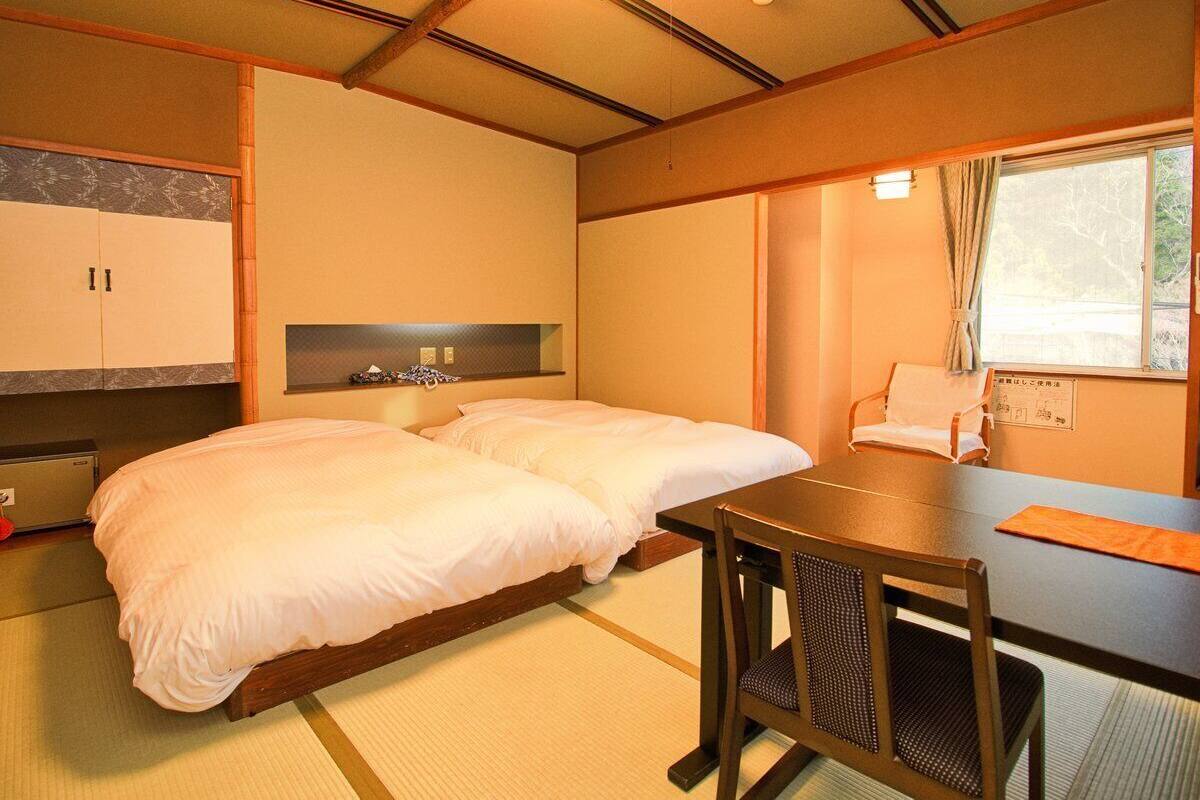 Ein Hotelzimmer mit zwei Betten, einem kleinen Tisch und einem Fenster mit Vorhängen.