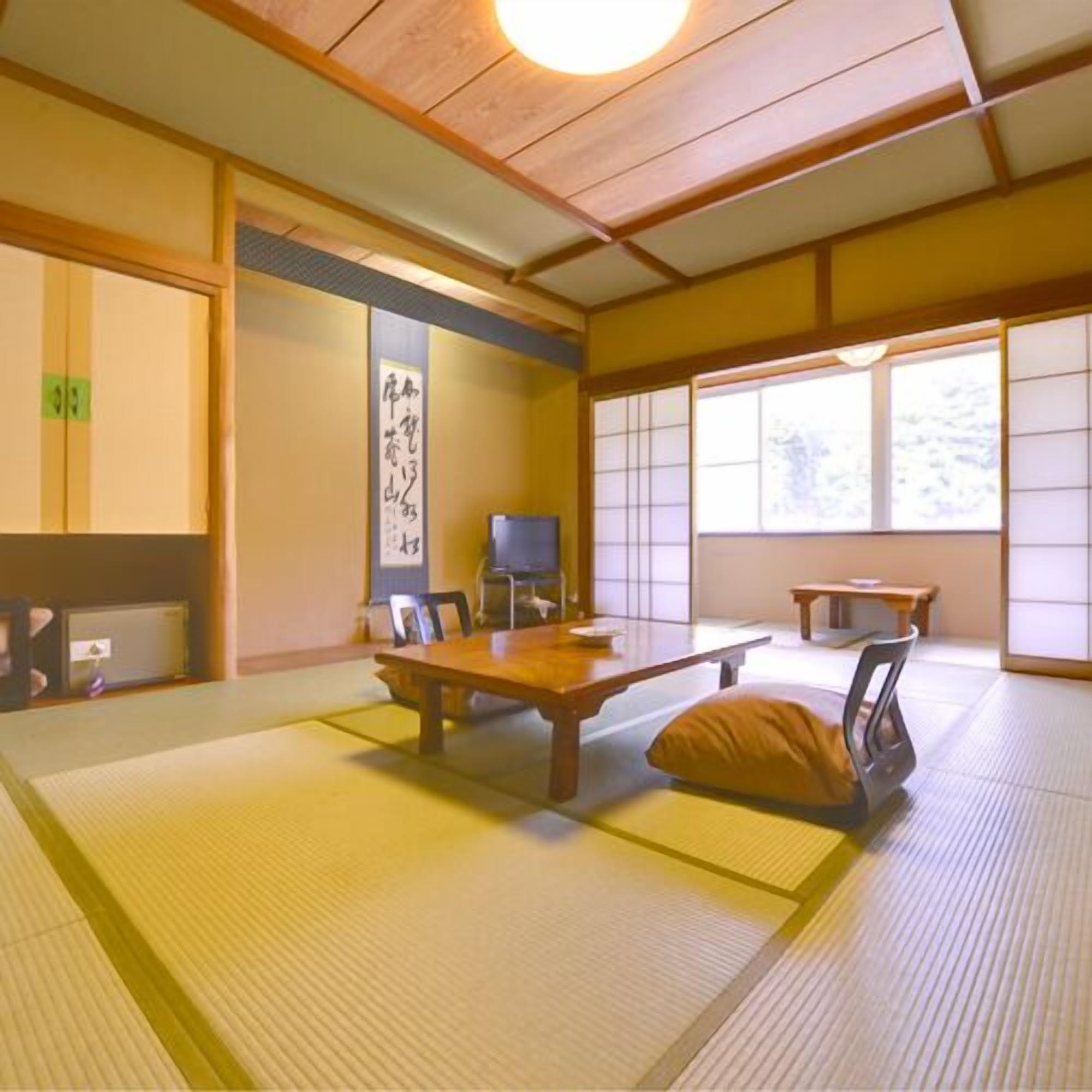 A traditional Japanese room with tatami flooring, a low table, chairs, a television, and a sliding door.