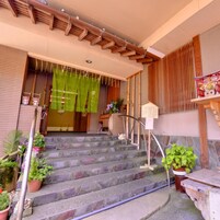 Una escalera conduce a la entrada de un edificio, con baranda de madera, plantas en macetas y un muro de bambú.