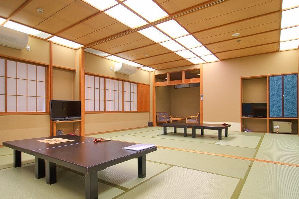 Ein Raum mit Tatami-Matten, Tatami-Boden, einem niedrigen Tisch, einem Fernseher und traditionellen Schiebetüren.