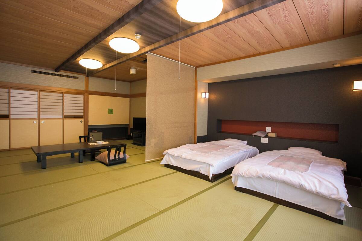 Ein traditioneller japanischer Raum mit Tatami-Bodenbelag, zwei Betten, einem niedrigen Tisch und einer Schiebetür.