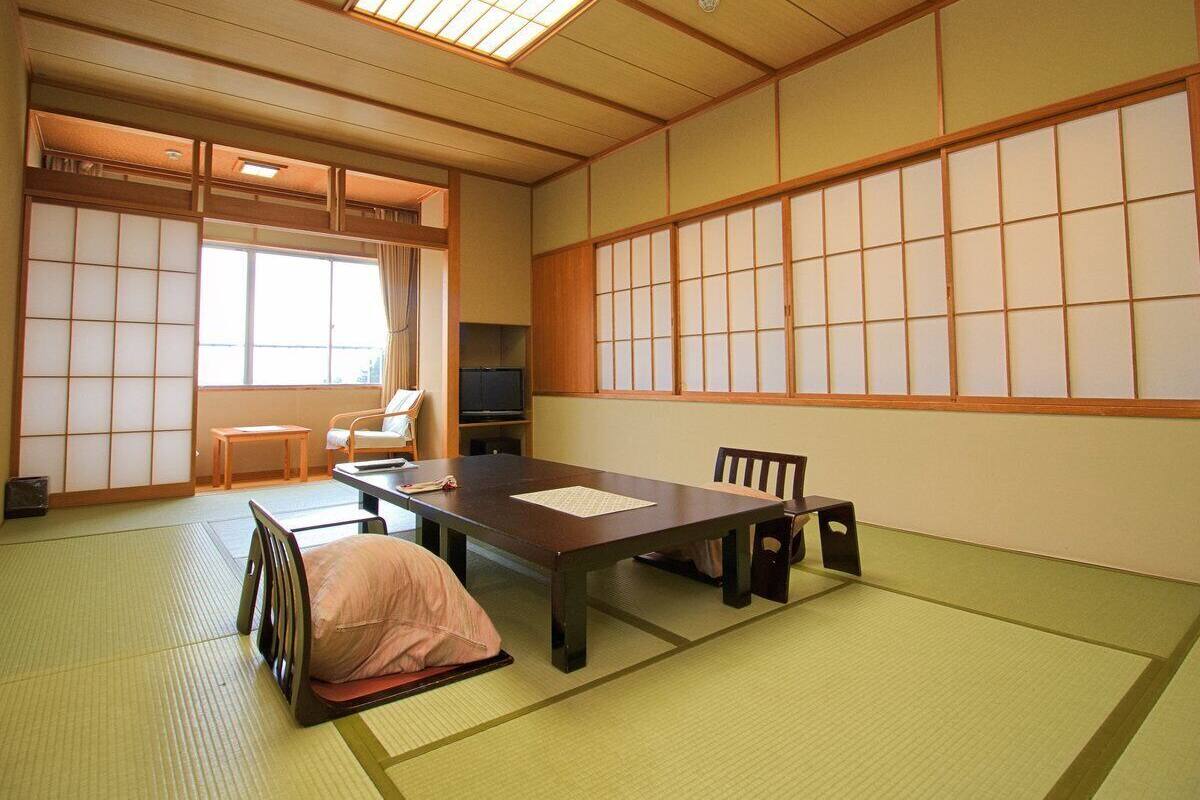 Ein traditioneller japanischer Raum mit Tatami-Boden, einem niedrigen Tisch, einer Couch und Schiebetüren.