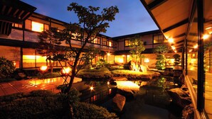 Un edificio de estilo japonés tradicional con un estanque de carpas koi, pasarelas de madera y ventanas iluminadas.