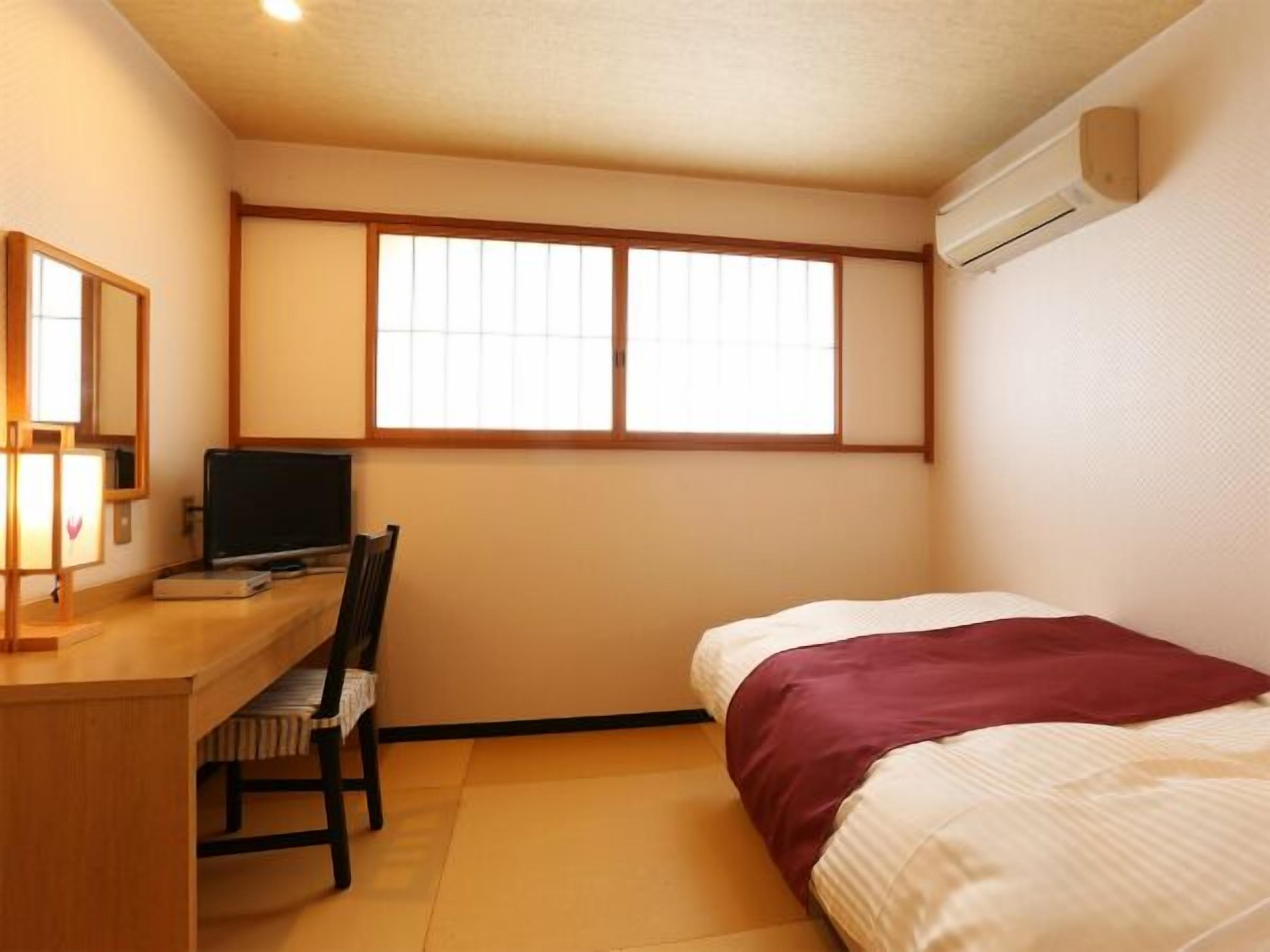 A small room with a bed, a desk, a chair, a TV, and a window.