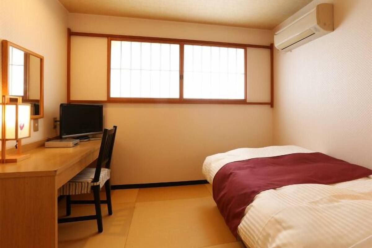 A small room with a bed, a desk, a chair, a TV, and a window.