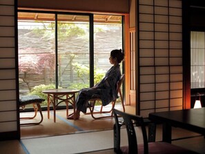 Una habitación con suelo de tatami, puertas correderas a un jardín y una mesa de estilo japonés tradicional.