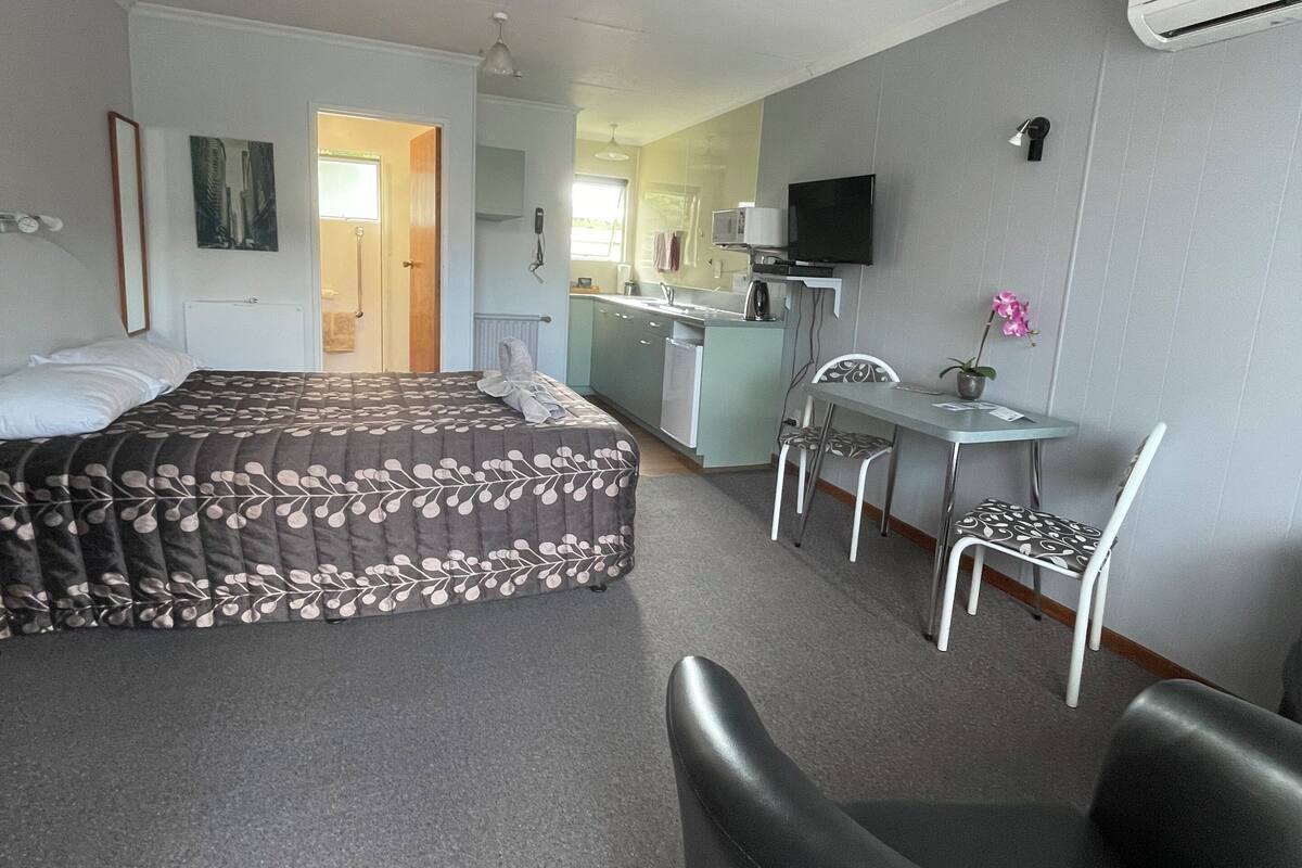 Una habitación de hotel compacta con cama, escritorio, silla y una kitchenette pequeña.