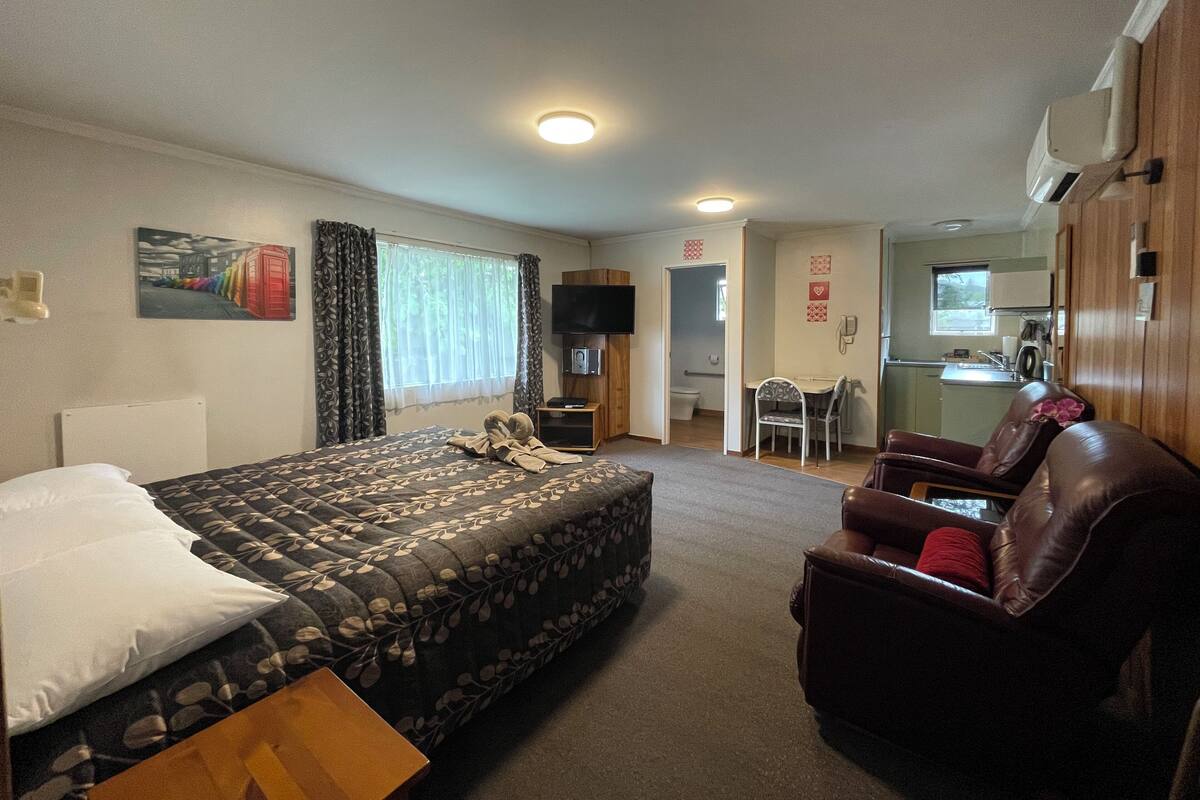 Una habitación de hotel con cama, una silla, escritorio y kitchenette.