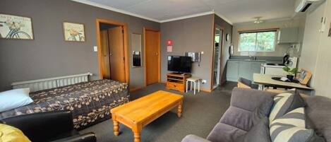 A compact living space with a sofa, a small table, a television, and a kitchenette in the background.