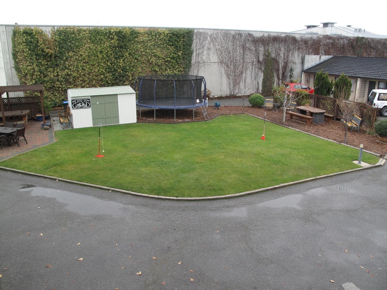 A backyard with a trampoline, a small shed, and a patio area with outdoor furniture.
