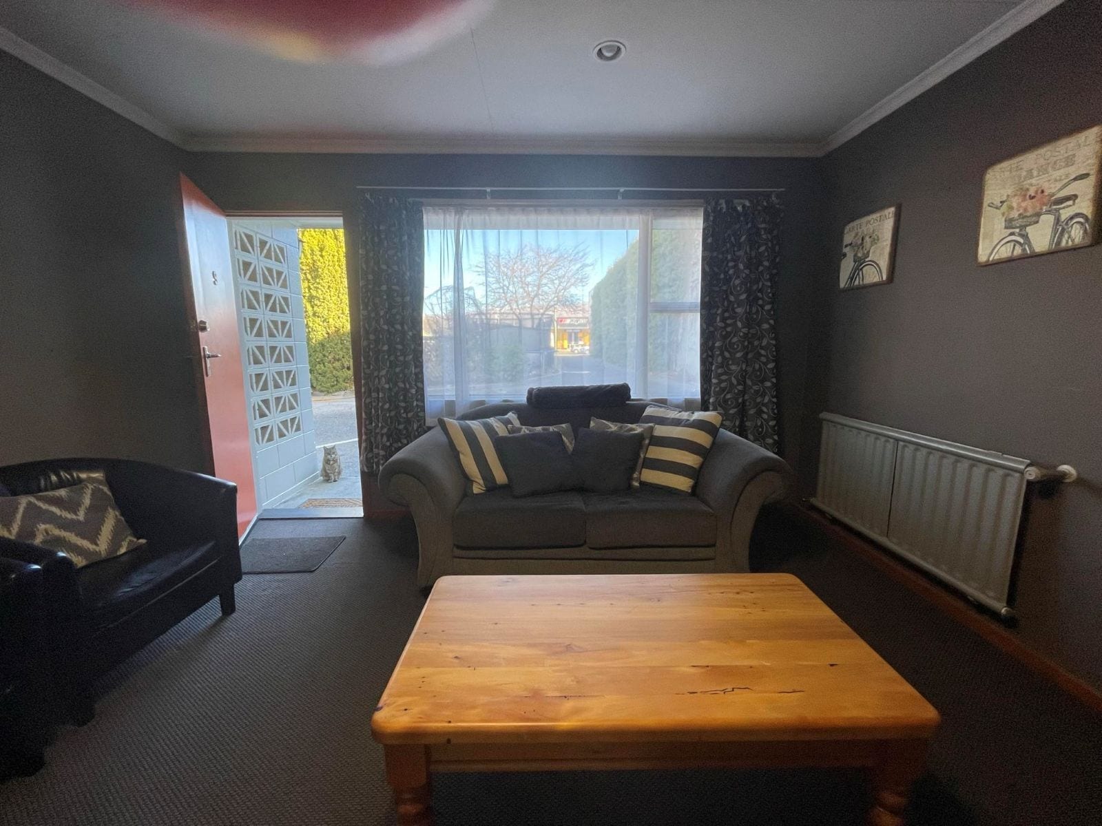 A living room with a sofa, a wooden coffee table, a black armchair, a window with curtains, and a radiator.