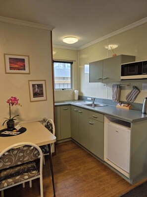 A compact kitchen with a dining area, a microwave, and a small refrigerator. - Alexandra Motor Lodge (Alexandra)