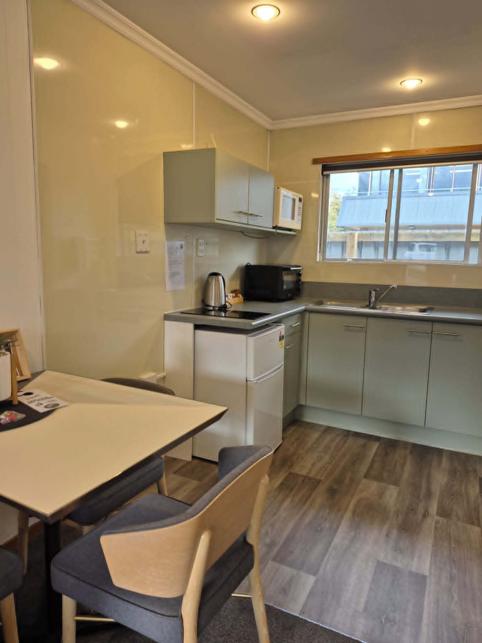 A compact kitchen with a microwave, kettle, and toaster, a small refrigerator, and a window with a view.