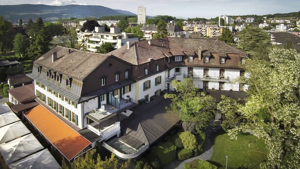 A large, multi-story building with a central courtyard, surrounded by trees and other buildings. - Hôtel La Prairie, Swiss Bike Hotels (Yverdon-les-Bains)