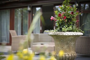 A stone planter with flowers and a wicker chair in the foreground.