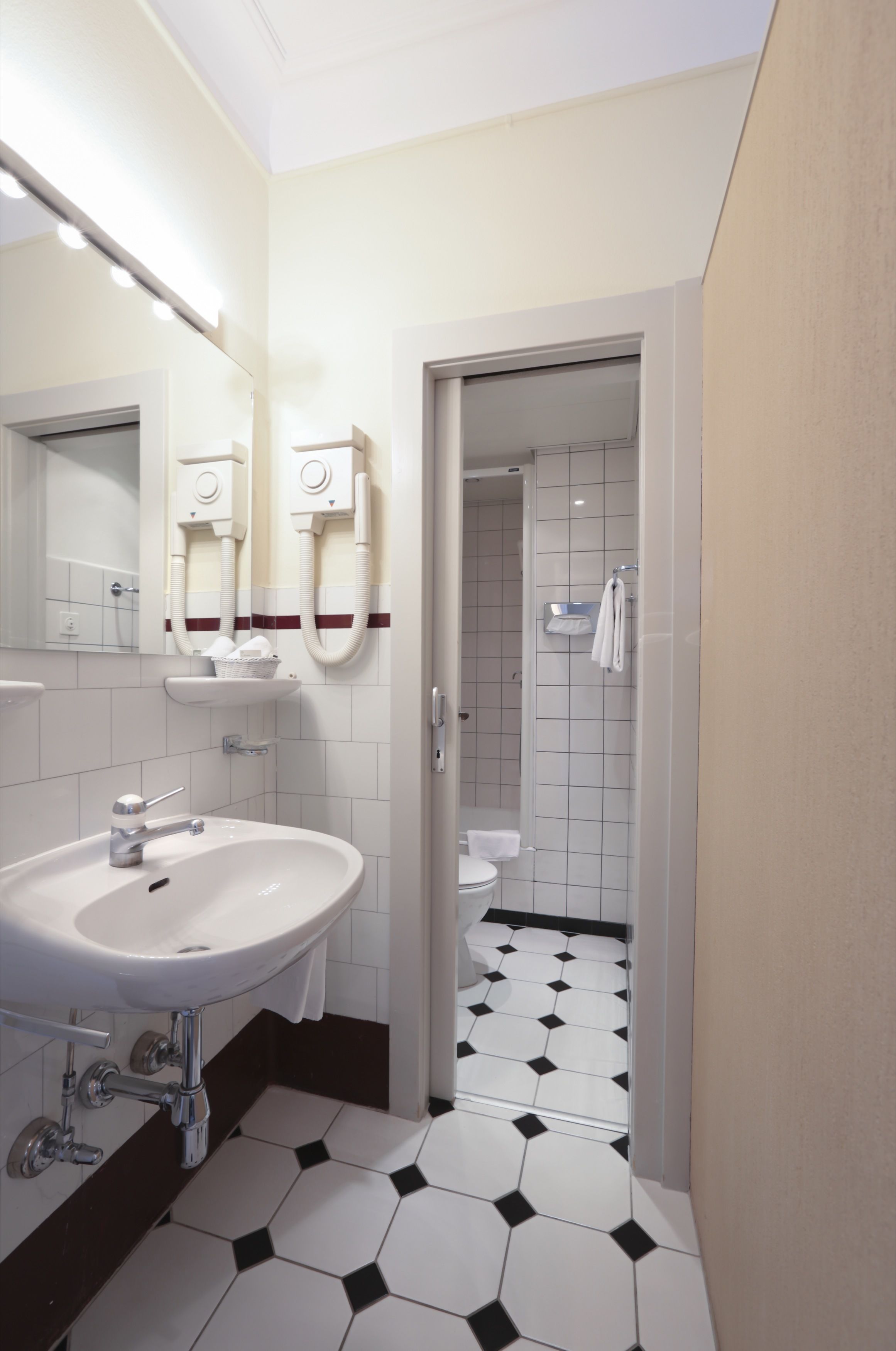 Une salle de bain avec un lavabo blanc, un miroir et un sèche-cheveux fixé au mur.