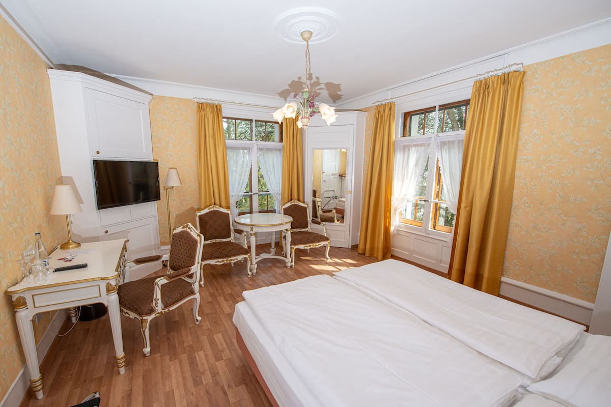 Een hotelkamer met een bed, een bureau met een televisie, een stoel, een tafel en gordijnen.