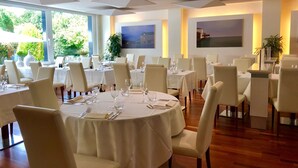 A dining area with round tables, white chairs, and a view of greenery outside. - Hôtel La Prairie, Swiss Bike Hotels (Yverdon-les-Bains)