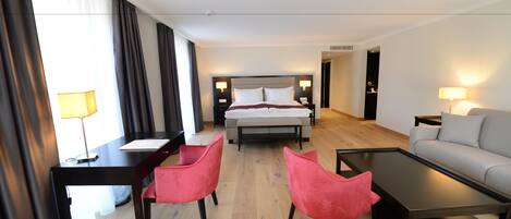 A hotel room with a bed, a desk, two chairs, a sofa, and a coffee table.