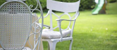Two white metal chairs with cushioned seats and backs, placed on a grassy lawn.