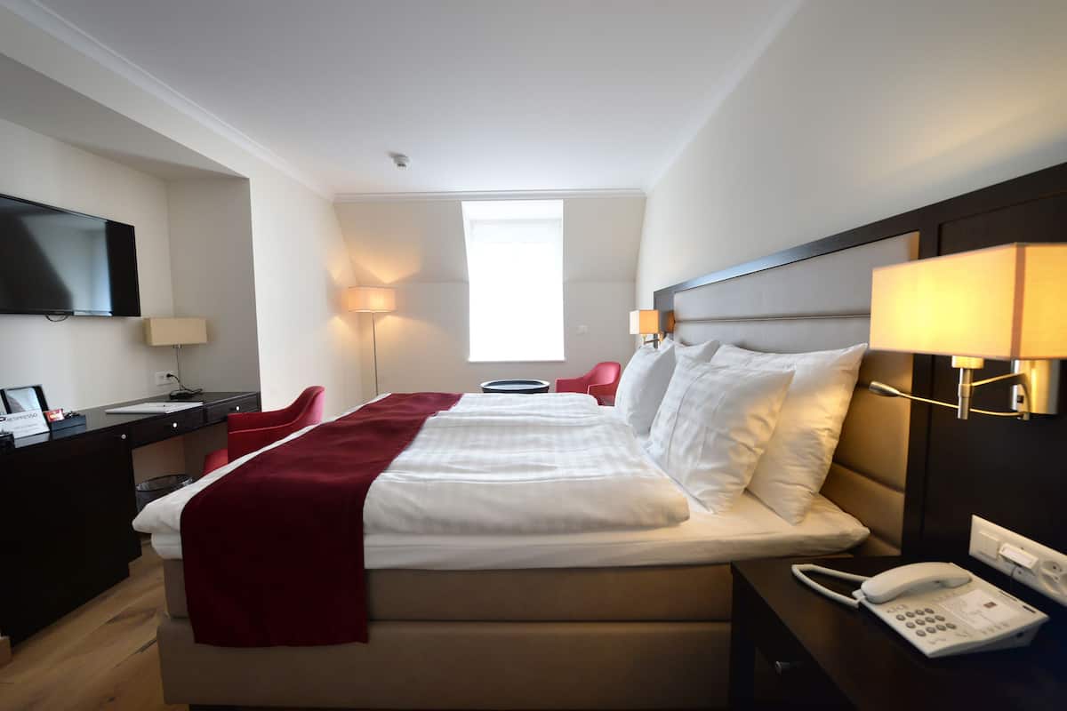 Hotelkamer met een bed, nachtkastje, lamp en bureau met een flatscreen-tv.