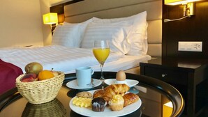 A hotel room with a neatly made bed, a breakfast tray with croissants, muffins, and fruit, and a glass of orange juice. - Hôtel La Prairie, Swiss Bike Hotels (Yverdon-les-Bains)