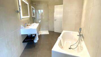 Un baño moderno con una bañera grande, zona de ducha separada y tocador con espejo.