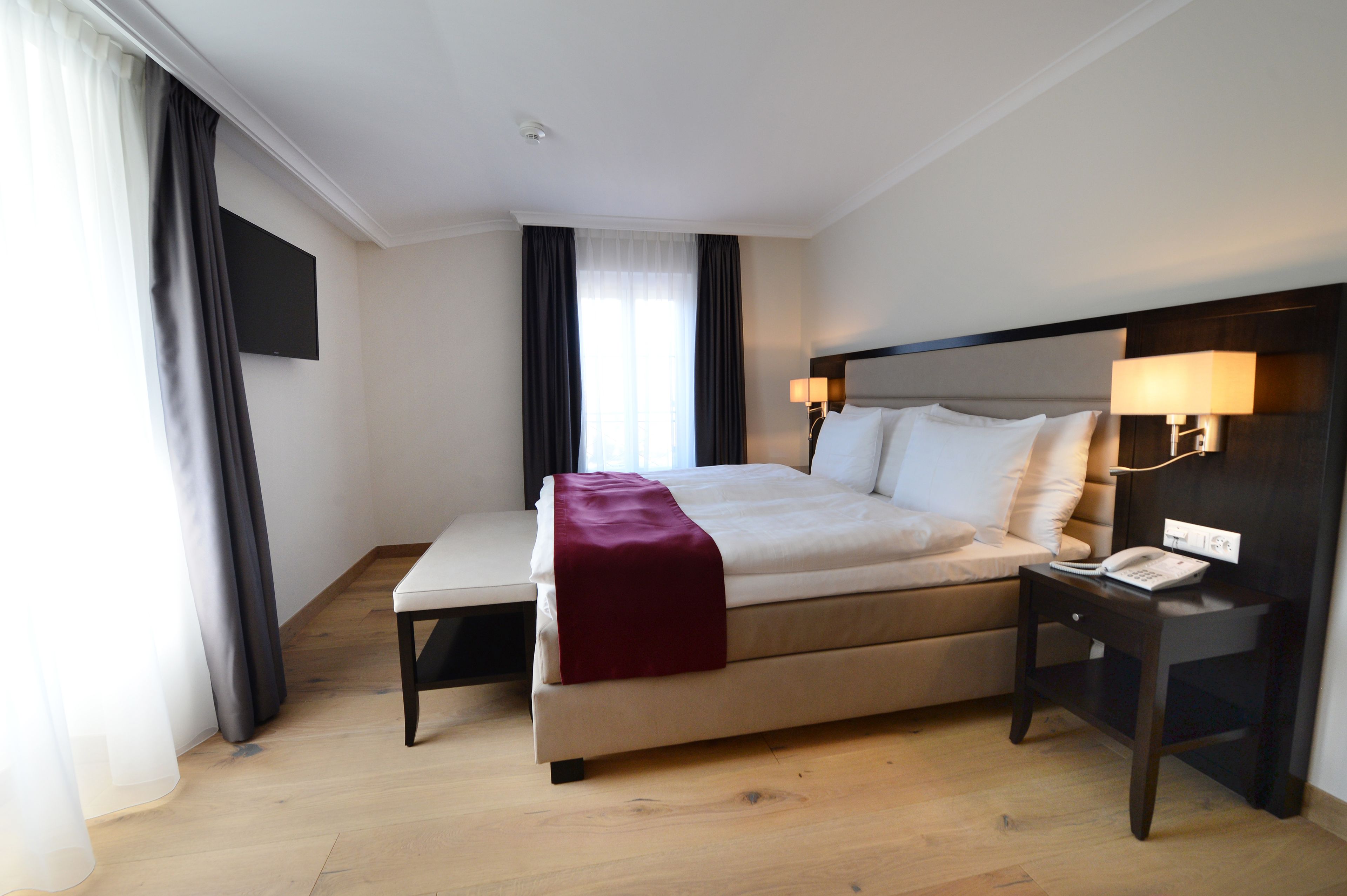A hotel room with a bed, bedside table, and a TV mounted on the wall.
