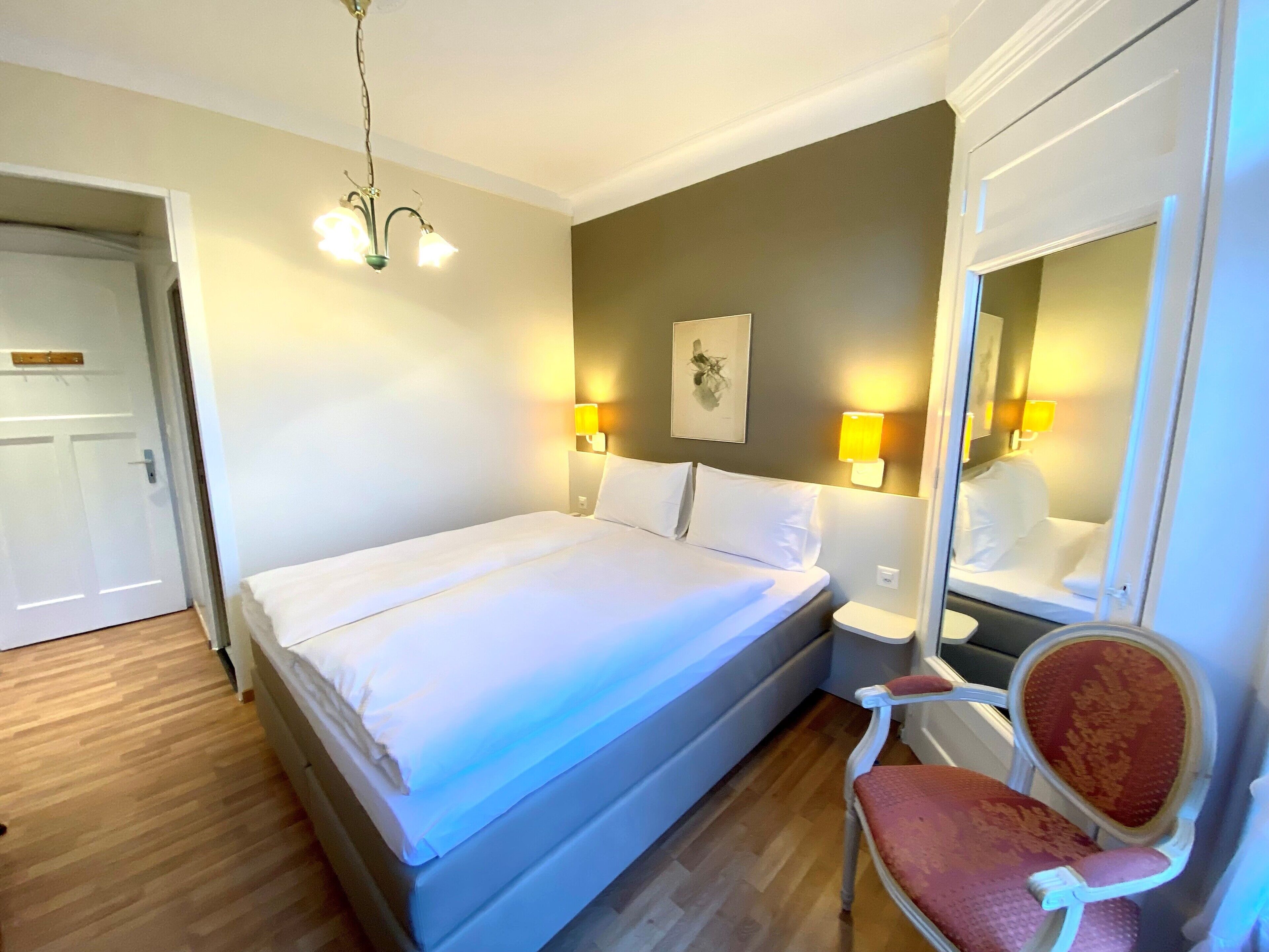 A hotel room with a bed, bedside lamps, a chair, and a mirror.