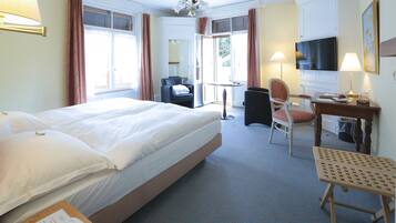 Et hotelværelse med en stor seng, et skrivebord med stol, et fjernsyn og et lille bord med lampe.