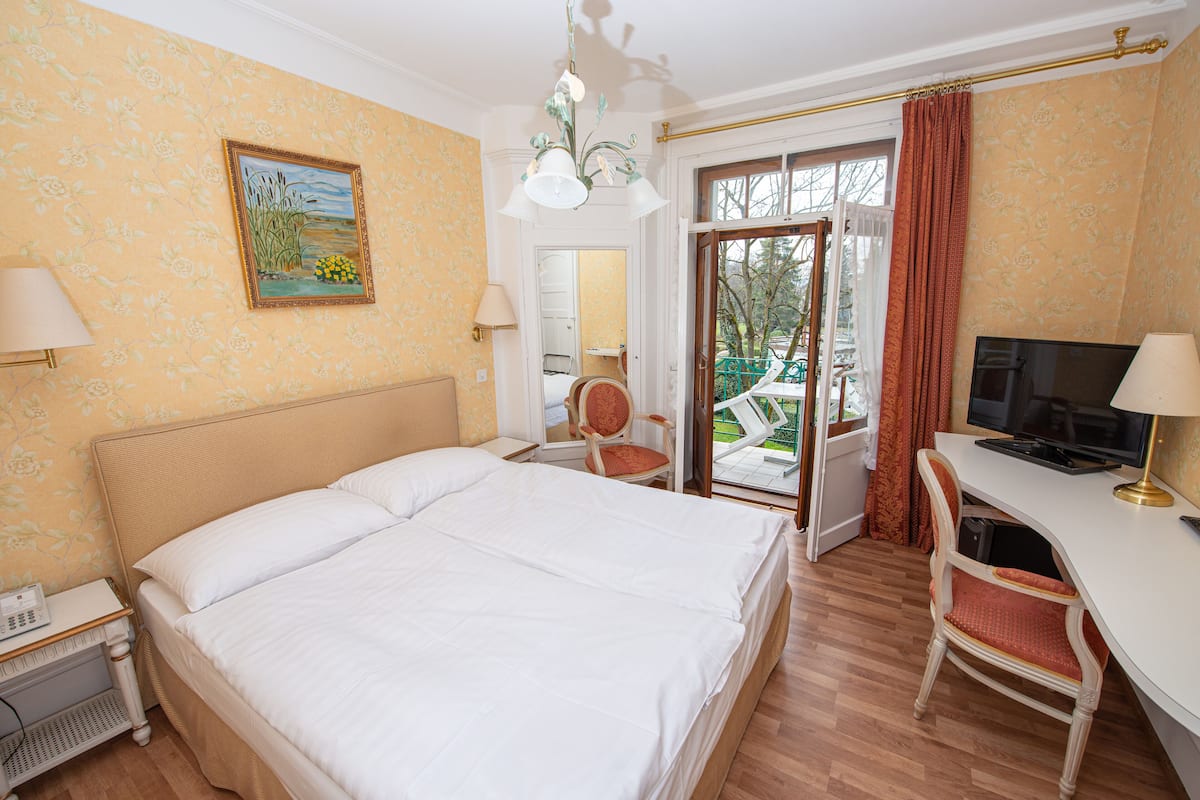 Hotelkamer met een groot bed, een bureau met computer, een stoel, een lamp en een schilderij aan de muur.
