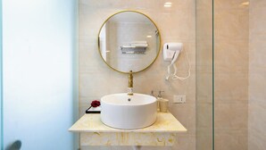 A bathroom with a round mirror, a white sink, a glass shower enclosure, and a telephone.