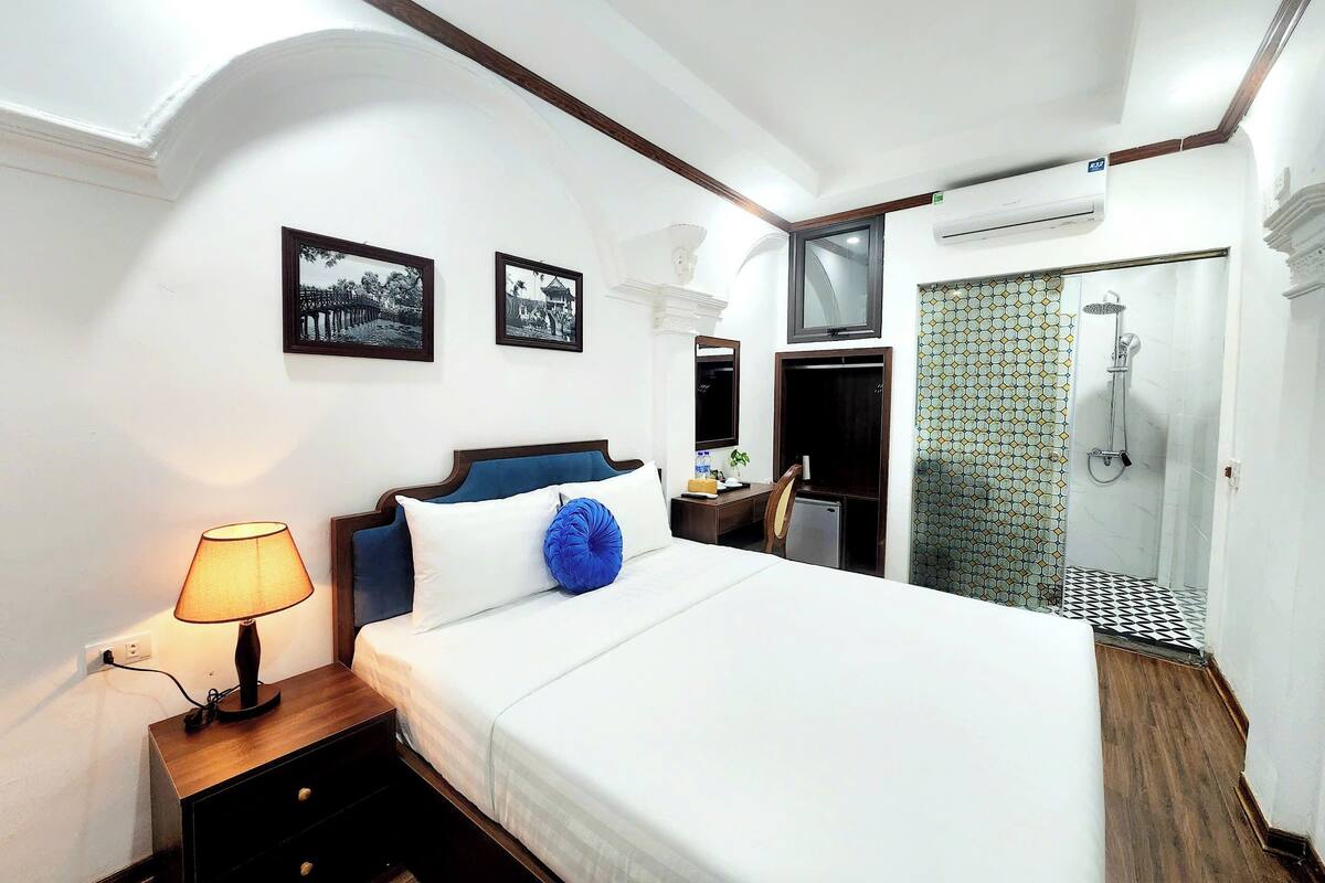 Ein Hotelzimmer mit Bett, Nachttischlampe, Schreibtisch, Stuhl und einer Duschkabine.
