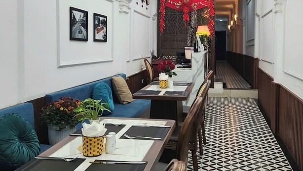 A hotel corridor with a blue sofa, a dining table set with black placemats, and a patterned floor.