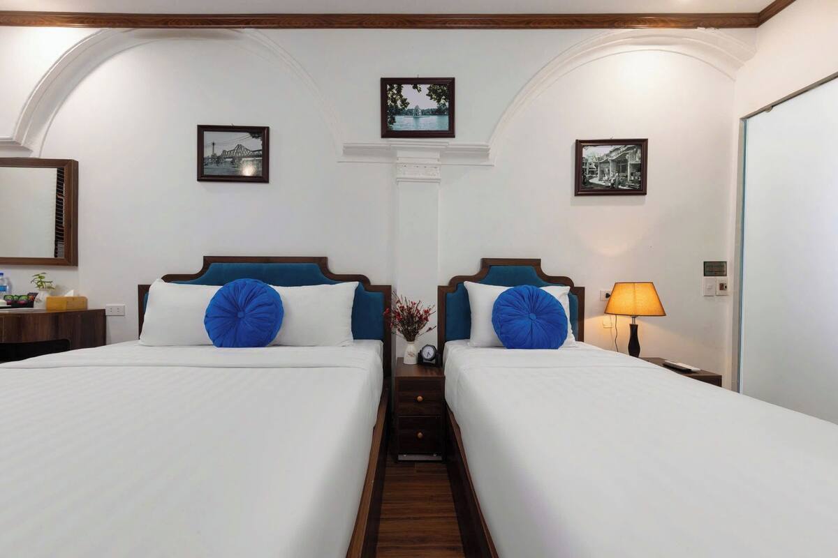 Ein Hotelzimmer mit zwei Betten, einem Nachttisch mit Lampe und gerahmten Bildern an den Wänden.