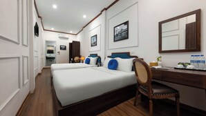 A hotel room with a large bed, a desk, a chair, a mirror, and a framed picture on the wall.