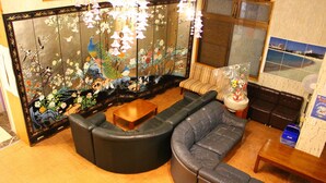 A living room with a sofa, a wooden coffee table, and a decorative screen with floral and peacock designs. - Shirahama Onsen Minshuku A Course (Shirahama)