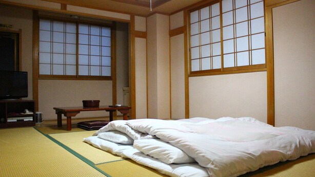 A traditional Japanese-style room with tatami flooring, a bed with white bedding, a television, and a small table with a bowl. - Shirahama Onsen Minshuku A Course (Shirahama)