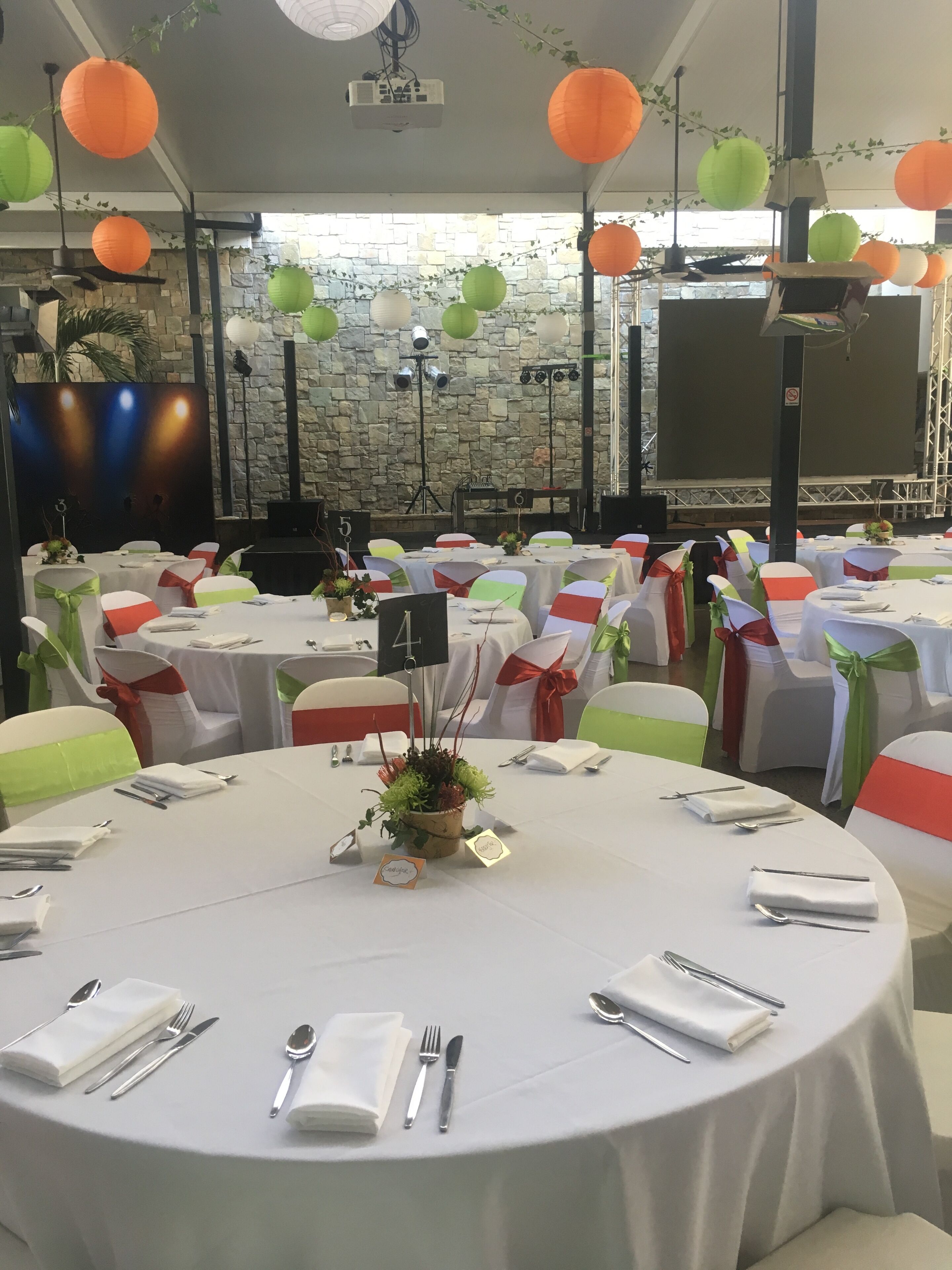 A banquet hall with round tables set for a formal event, decorated with white tablecloths and green and red sashes.