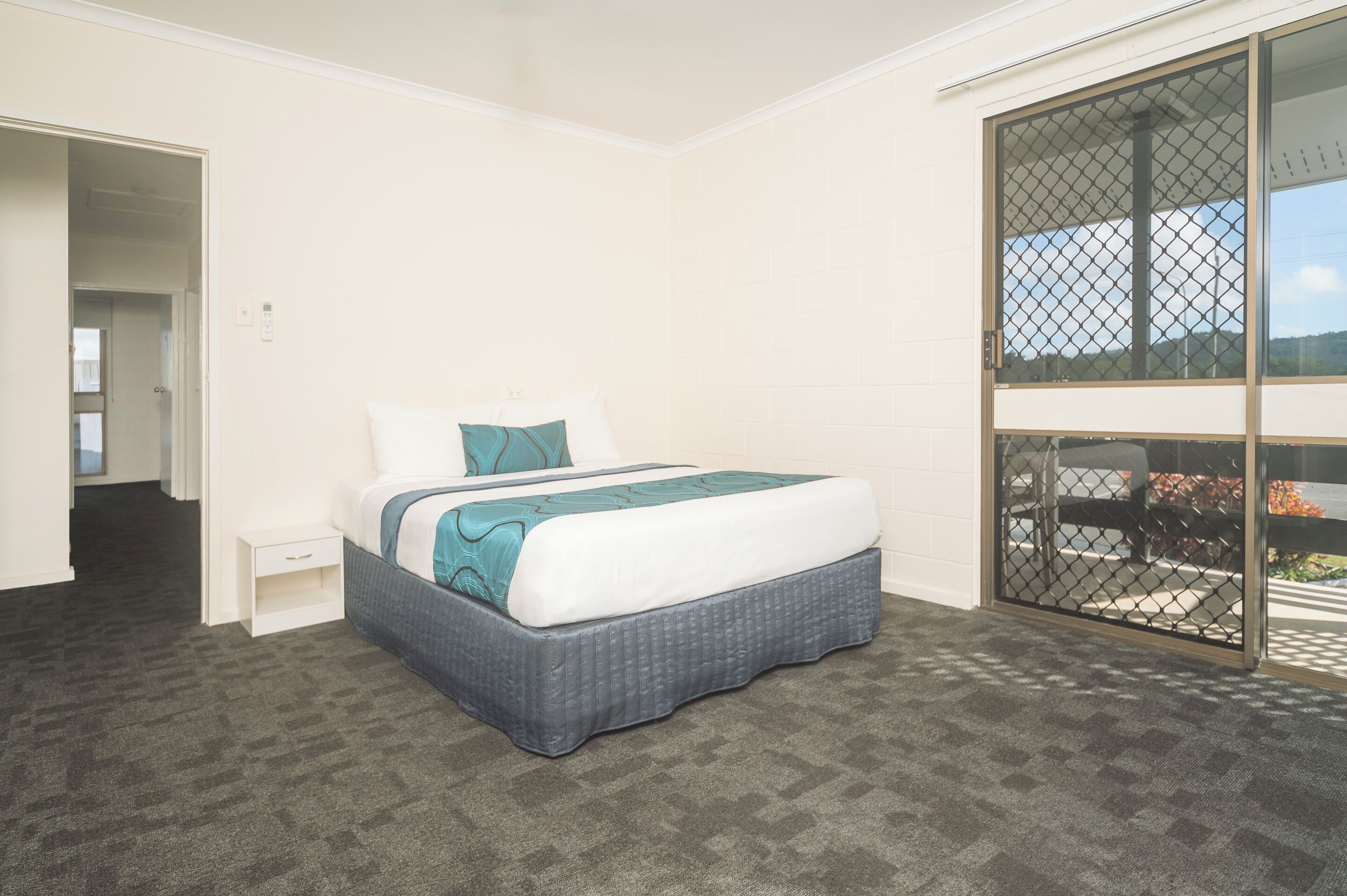 A bedroom with a bed, a small bedside table, and a large sliding glass door leading to an outdoor area.