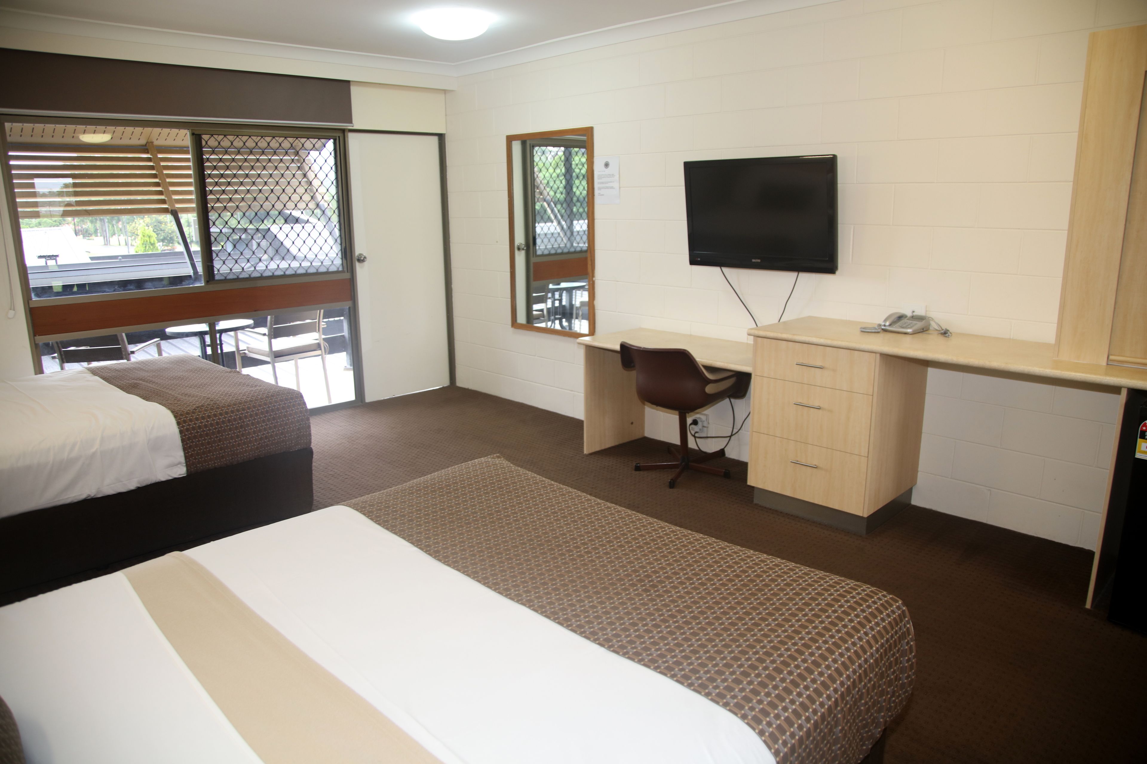 A hotel room with two beds, a desk, a chair, a television, and a window with blinds.
