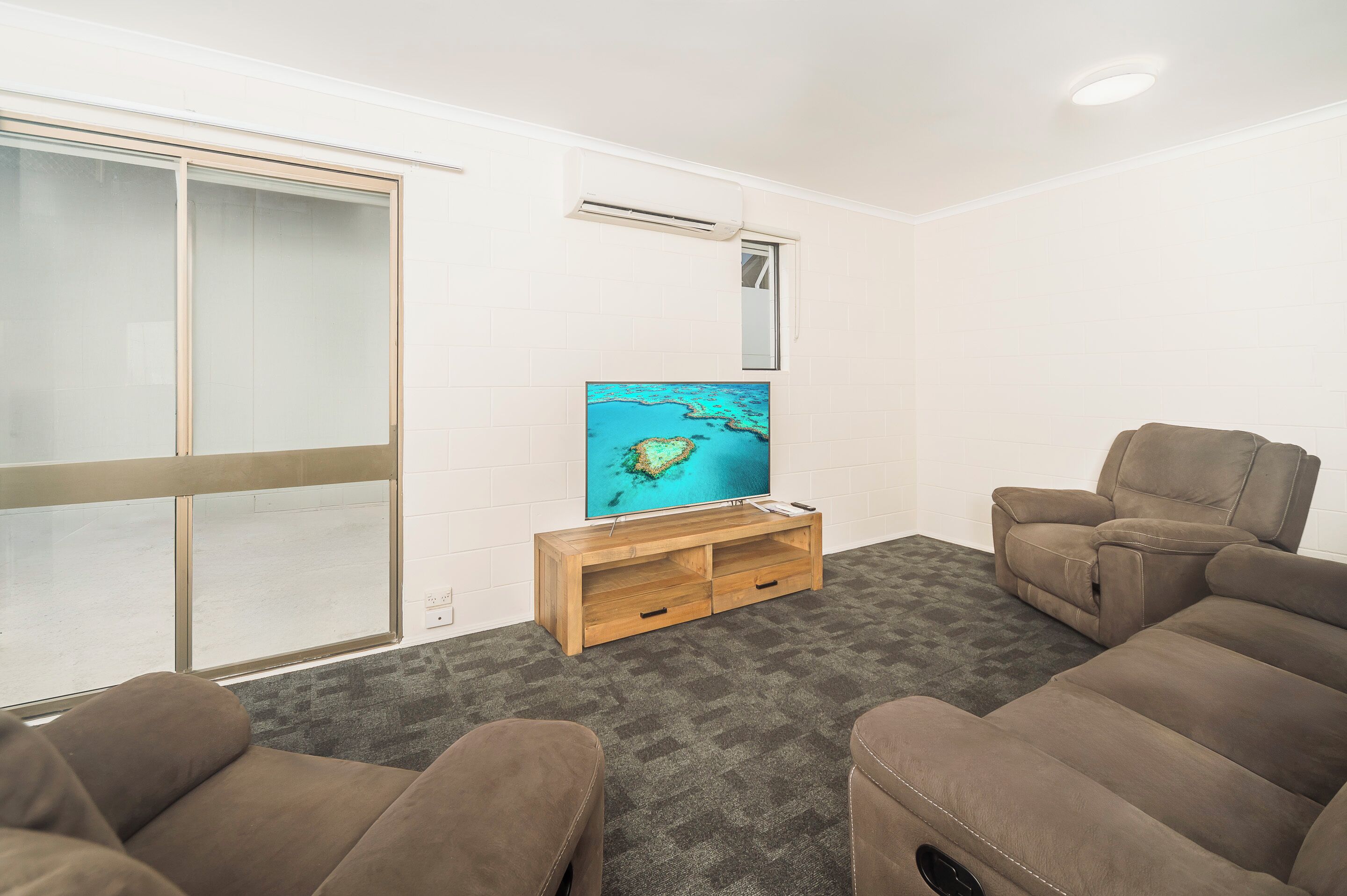 A living room with a large flat-screen TV, a sliding glass door, and two brown sofas.