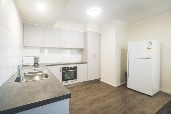 A modern kitchen with white cabinets, a stainless steel sink, and a built-in oven. - Cannonvale Reef Gateway Hotel (Cannonvale)
