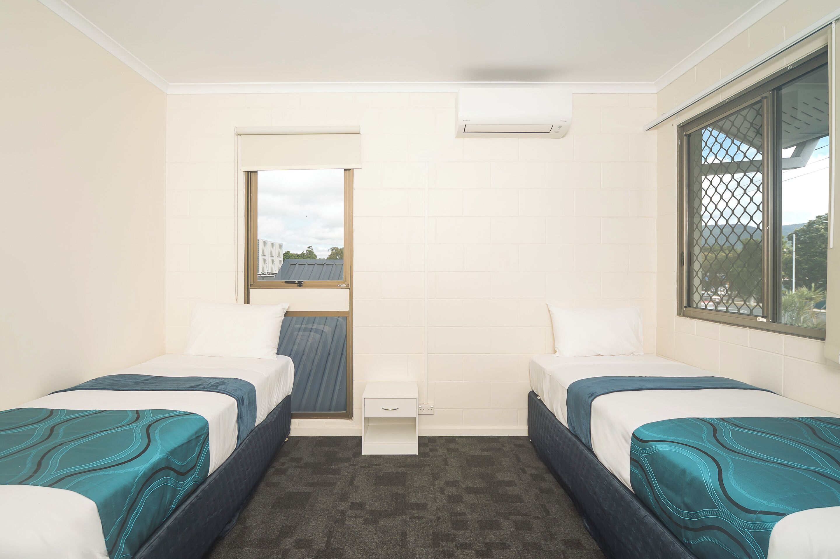 A small, clean room with two beds, a small table, and a window with a view.