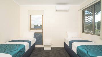 A small, clean room with two beds, a small table, and a window with a view.