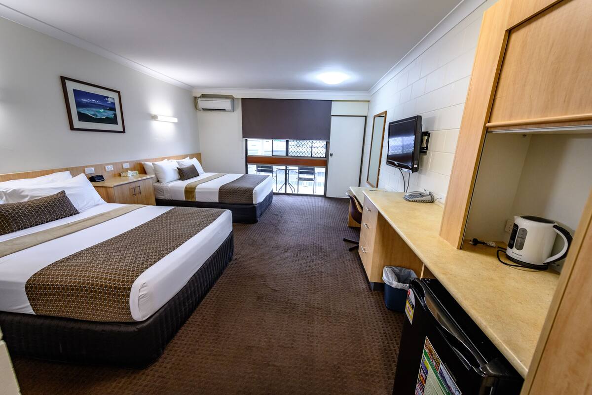 A hotel room with two beds, a desk, a television, and a window with a view.