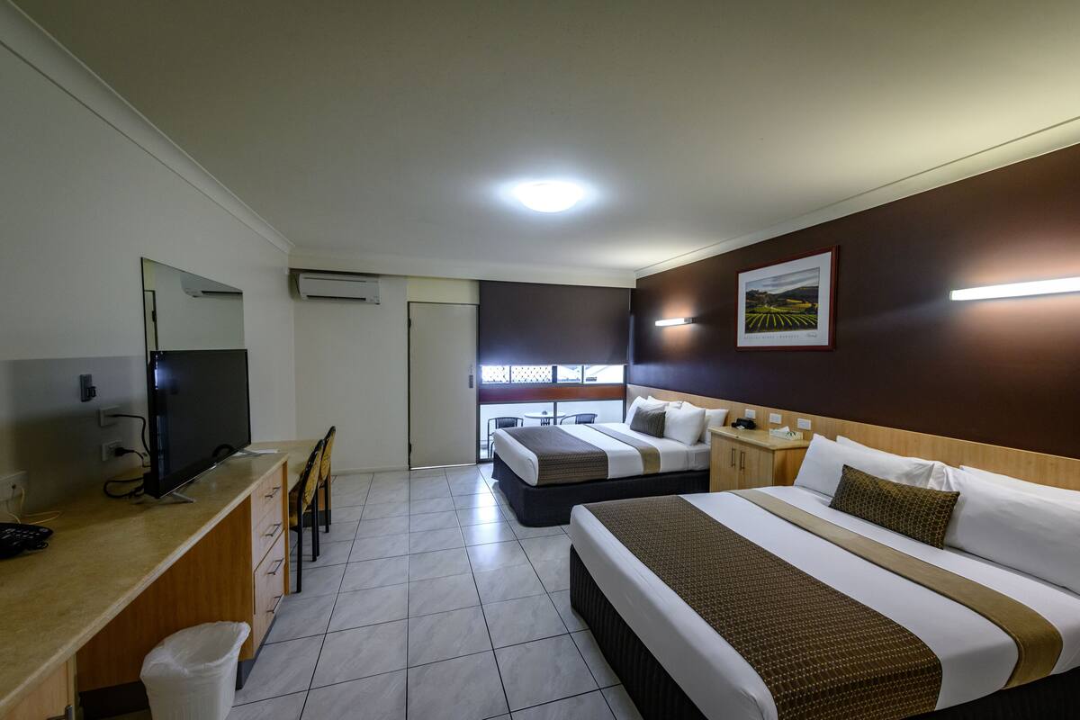 A hotel room with two beds, a desk with a TV, and a view of the outside balcony.