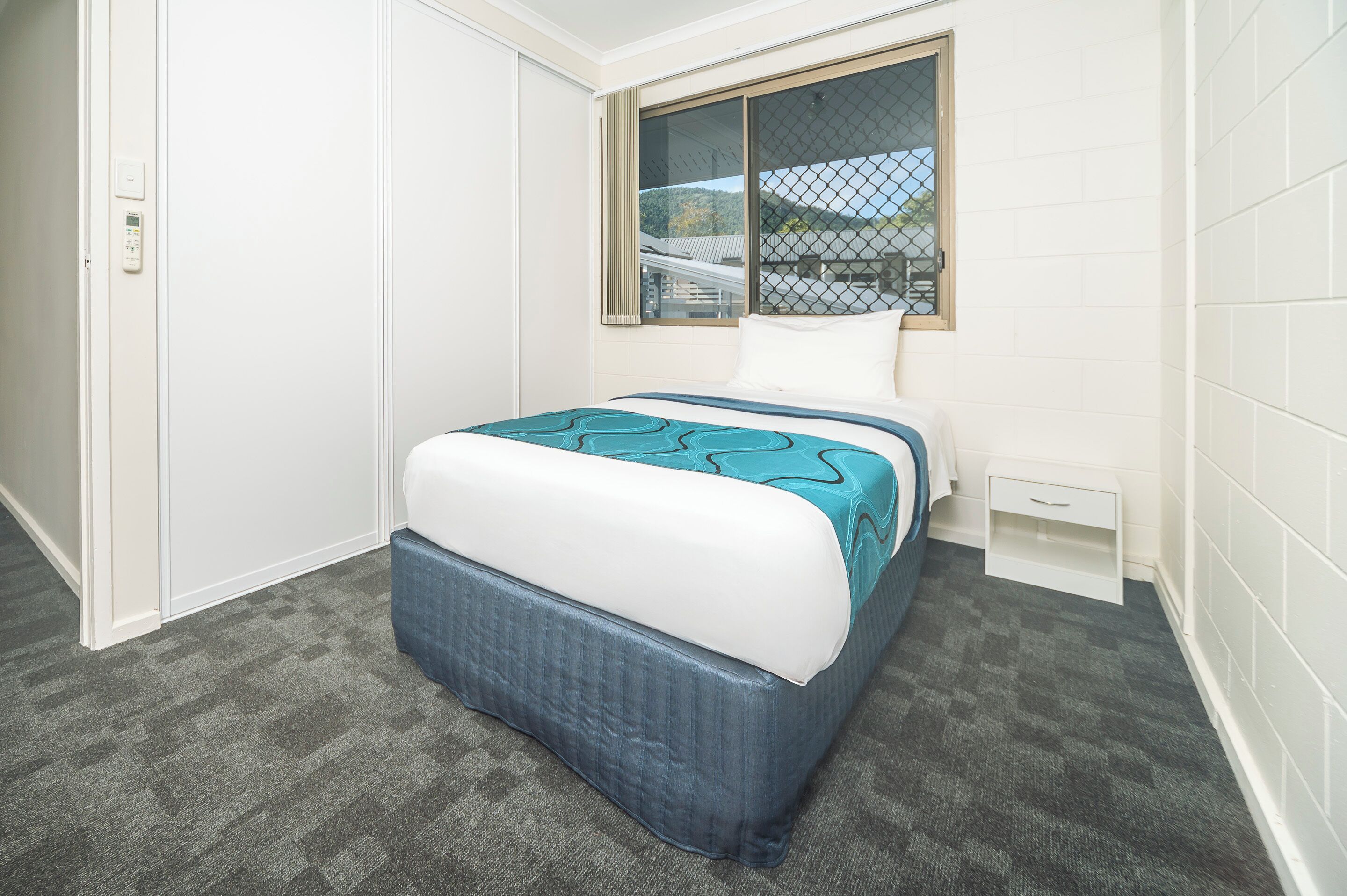 Un dormitorio con cama, ventana, mesita de noche y piso alfombrado.