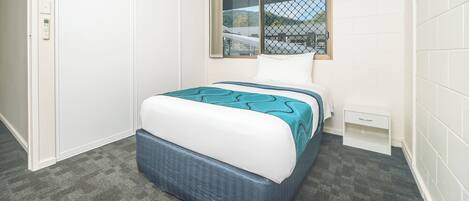 Un dormitorio con cama, ventana, mesita de noche y piso alfombrado.