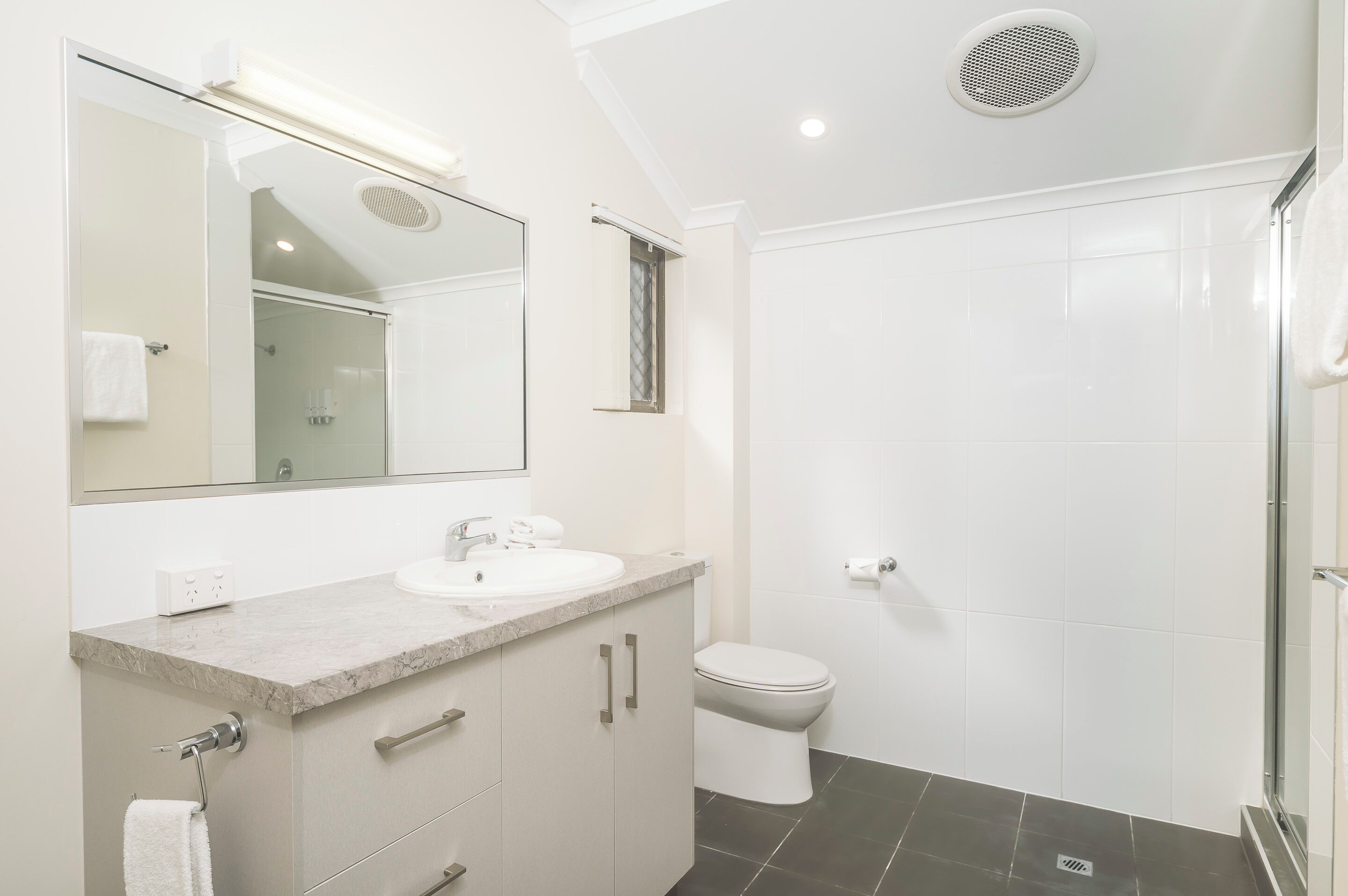Un baño moderno con encimera de mármol, inodoro y cabina de ducha con paredes de vidrio.